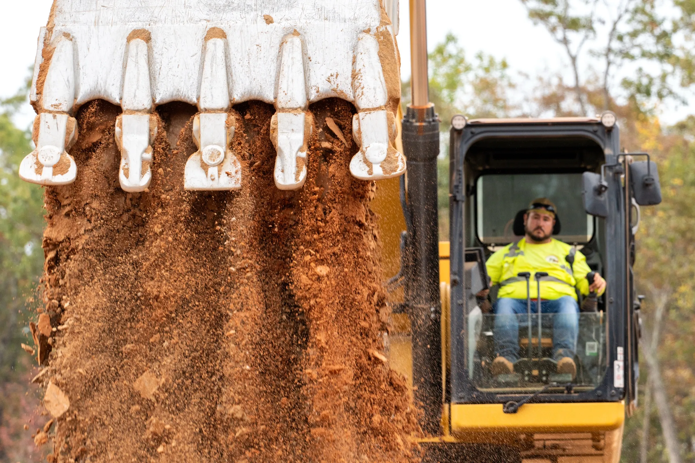 An excavator operator in hi-vis works the controls as soil pours from the bucket