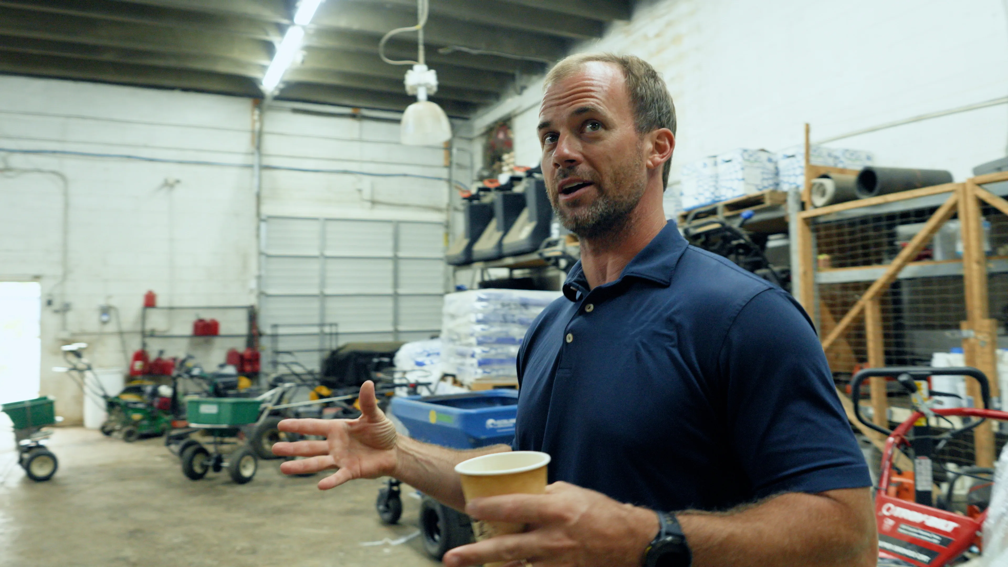 A business owner in a navy polo talks with his hands in his equipment shop